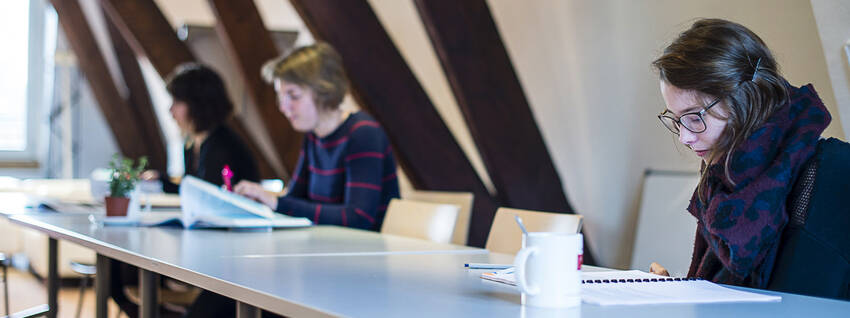 Drie personen die aan lange tafel documenten doornemen