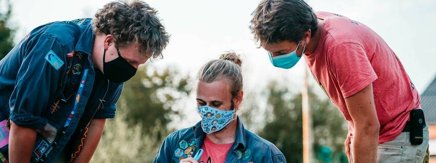 Drie personen met mondmasker kijken samen in een kaft