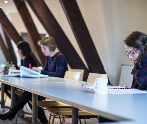 Drie personen die aan lange tafel documenten doornemen